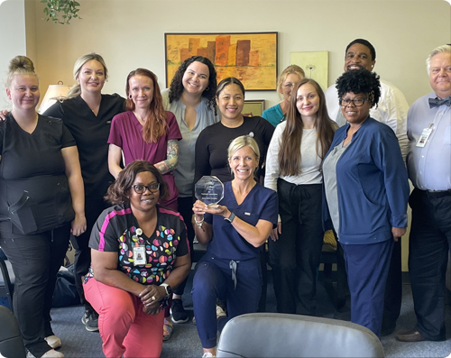 A diverse group of healthcare professionals from James River Home Health & Hospice posing together in an office setting, with two women in the foreground holding a glass excellence award.
